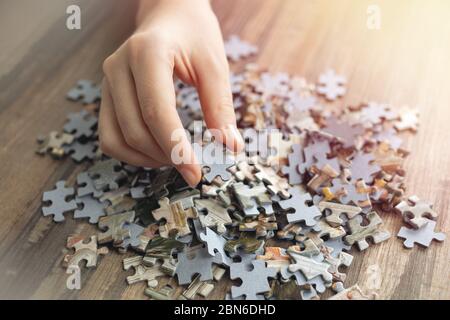 Hand picking one piece of mixed jigsaw puzzle, macro close up. Problem solving concept Stock Photo