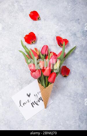 Ice cream of red  tulip flowers in waffle cone with card Love you mom  on concrete  table top view in flat lay style. Stock Photo