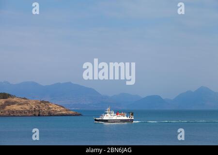 A small Caledonian MacBrayne ferry arriving into Loch Scresort on the Isle of Rum on the west coast of Scotland with the Skye Cuillin behind. Stock Photo