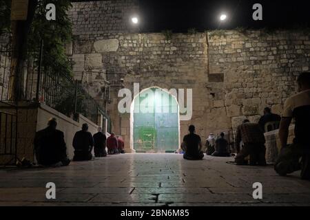 Muslim worshipers perform the Taraweeh prayer in front of the closed gates of Bab al-Asbat ( the Gate of the Tribes ) outside al-Aqsa mosque compound during the Muslim holy month of Ramadan in the Old City of Jerusalem amid the COVID-19 pandemic on May 12, 2020. The Al-Aqsa Mosque, located on the Temple Mount plaza in Jerusalem, was closed 51 days ago by the Waqf, the religious body that manages Muslim holy sites in the Holy City, an exceptional measure aimed at curbing the Coronavirus pandemic. Stock Photo