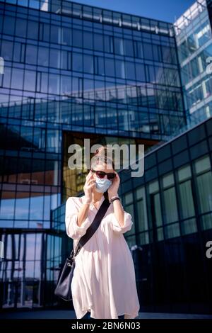 Shot of attractive woman wearing face mask and looking careworn while talking with somebody on her mobile phone on the street. Stock Photo