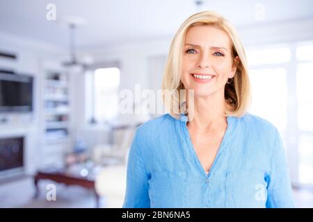 Portrait of beautiful blond woman looking at camera and smiling while standing in the living area at home. Stock Photo