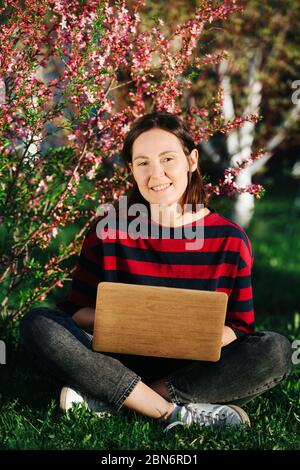 Beautiful girl with a laptop, she works sitting in a flowering garden  Stock Photo