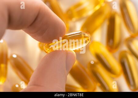 Fingers holding a capsule of cod liver oil, selective focus Stock Photo