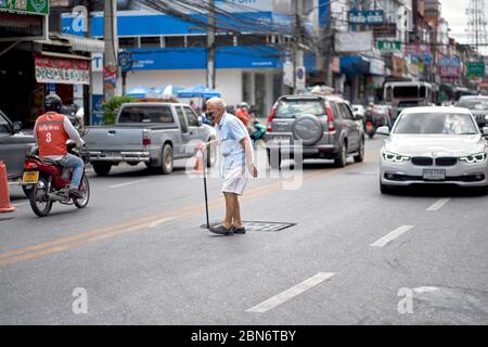 Elderly man with a walking stick attempting to cross the road with heavy traffic. Thailand Southeast Asia Stock Photo