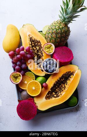 Tropical fruits flat lay with mango, papaya, pitahaya, passion fruit, grapes, limes and pineapples on a tray. Table with ingredients for summer snacks Stock Photo