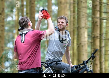 Two downill mountainbikers giving a high five to each other after successful run Stock Photo