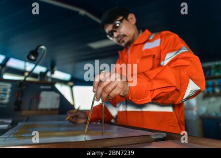 Filipino deck Officer on bridge of vessel or ship. He is plotting position on chart Stock Photo