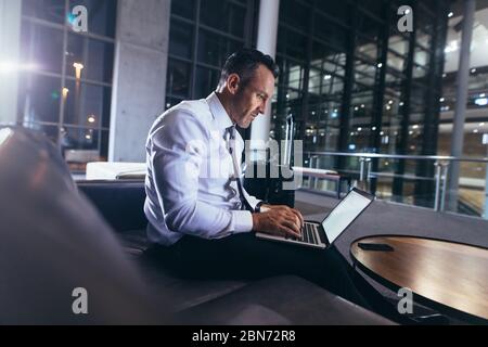 Businessman waiting at the airport using laptop. Man in formalwear sitting at airport departure area using his laptop. Stock Photo