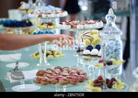 Female hands taking cakes with a tongs from a banquet table laid with sweets Stock Photo