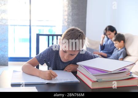 Children doing homework at home. Mother helping her son with homework and works online with laptop computer Stock Photo
