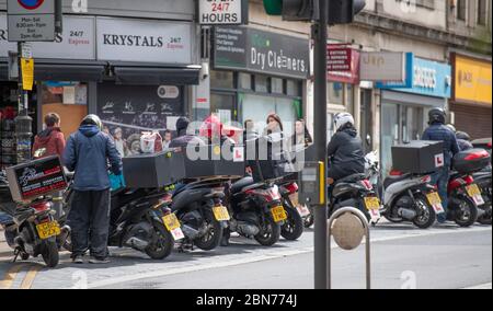 Wimbledon, London, UK. 13 May 2020. On day 51 of Coronavirus lockdown in the UK some businesses reopen and workers who cannot work from home are encouraged to travel to work by bike or walking if possible. Scooter take-away drivers wait for business outside Wimbledon Station. Credit: Malcolm Park/Alamy Live News. Stock Photo