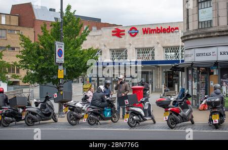 Wimbledon, London, UK. 13 May 2020. On day 51 of Coronavirus lockdown in the UK some businesses reopen and workers who cannot work from home are encouraged to travel to work by bike or walking if possible. Scooter take-away drivers wait for business outside Wimbledon Station. Credit: Malcolm Park/Alamy Live News. Stock Photo