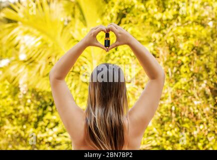 Woman hold in hands the bottle of essential oil on yellow natural background, view from the back. Stock Photo