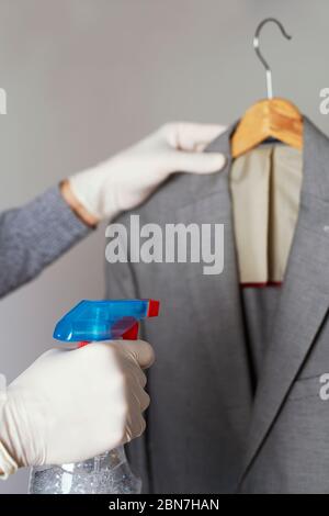 closeup of a man, wearing latex gloves, disinfecting a sport jacket hanging on a clothes hanger by spraying a disinfectant from a bottle Stock Photo