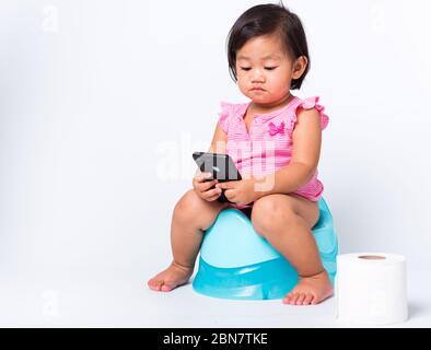 Asian little cute baby child girl education training to sitting on blue chamber pot or potty and play smart mobile phone with toilet paper rolls, stud Stock Photo