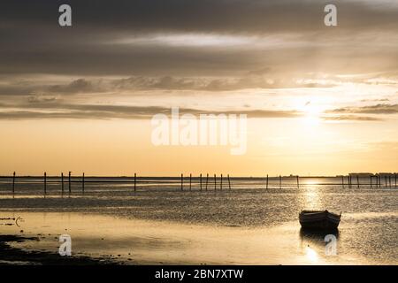 silhouette of a traditional fisherman wooden boat at sunset in the bay of cadiz, the sun reflects on the calm surface of the water, concept of peace a Stock Photo