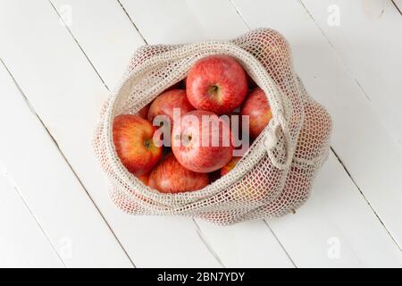 Apples in eco bag on white wooden background. Zero waste, eco friendly or plastic free lifestyle concept.  Stock Photo