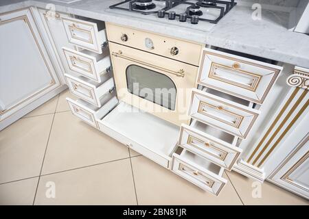 Interior of modern kitchen in classic style with golden elements in beige colors with built-in appliances. Drawer for plates or dishes shelf under the Stock Photo