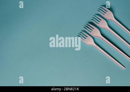 Four plastic forks on a light turquoise background. New white forks in a line. Minimalistic multitask background. View from above. Stock Photo