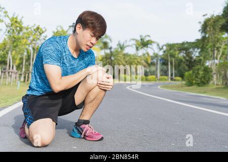 Asian man use hands hold on his knee injury while running on road in the park, Injury from workout concept. Stock Photo