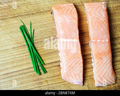 Two raw salmon fillets on a wooden chopping board with fresh chives Stock Photo