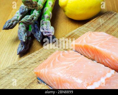 Two raw salmon fillets on a wooden chopping board with asparagus and lemon Stock Photo