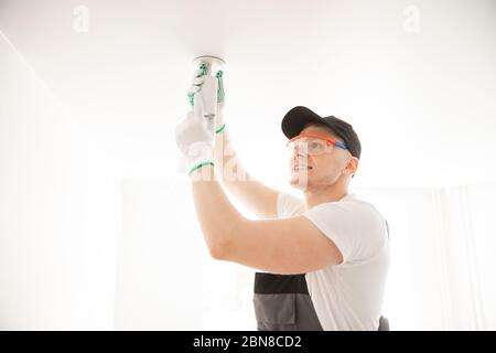 Electrician worker man assembling electric lamps in new apartment Stock Photo