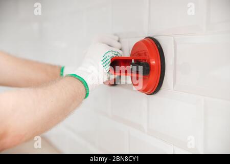Ceramic tile with chamfer hands in process of laying white rectangular tiles on kitchen wall Stock Photo