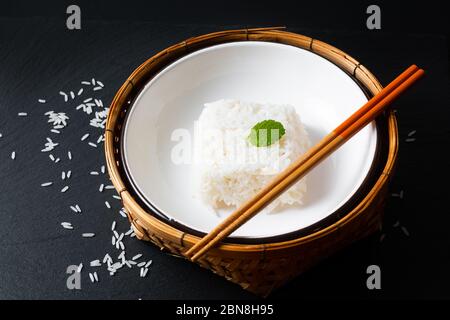 Asian Food concept cooked Thail jasmine rice long grain rice in ceramic bowl and bamboo tray on black slate board background with copy space Stock Photo