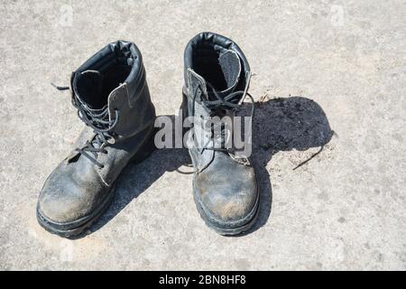 Pair of old used work boots on concrete background. Dirty black leather boots from the army Stock Photo