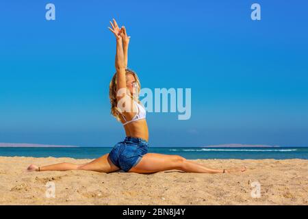 Young blonde dutch woman  practices yoga on beach Stock Photo