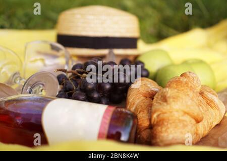 Picnic on the grass with croissant, pink wine, straw hat, grape on yellow plaid and green grass. Summer time Stock Photo