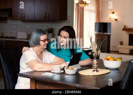 Caring nurse showing a digital tablet to an elderly woman in a nursing home. Spending time together. Stock Photo