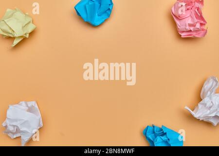 Crumpled pieces of paper of different colors on an orange background with copy space. Close up. Stock Photo