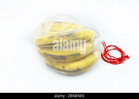 Ripe bananas packed in a white reusable mesh bag with red string, isolated on a white background. Stock Photo