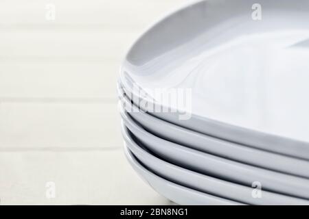 Stack pile of rectangular white ceramic dishes with rounded edges on wooden white background. Set group of classic porcelain shiny clean bowls. Stacke Stock Photo