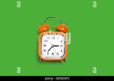 orange alarm clock on the green surface Stock Photo