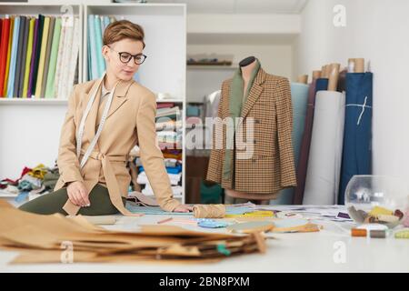 Young tailor working at her workplace with patterns she is going to make a new jacket in workshop Stock Photo