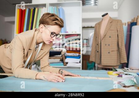 Young designer in eyeglasses drawing pattern on fabric at the table in workshop Stock Photo