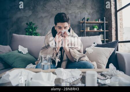 Portrait of his he nice attractive sick weak guy sitting on divan blowing nose suffering weakened immunity at modern industrial loft concrete brick Stock Photo