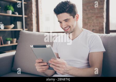 Close-up portrait of his he nice attractive focused funky cheerful cheery glad guy sitting on divan reading digital ebook finding job vacancy at Stock Photo