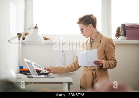 Young fashion designer working with sketches of new collection in her workplace at office Stock Photo