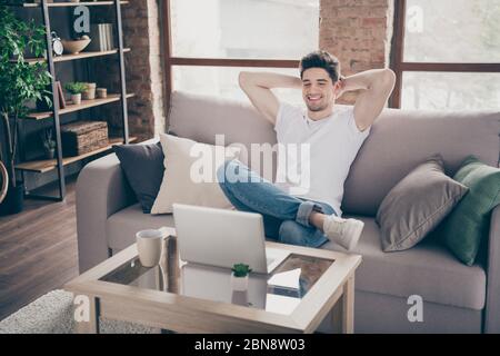 Portrait of his he nice attractive muscular cheerful cheery guy sitting on divan resting working remotely part-time at modern industrial loft interior Stock Photo