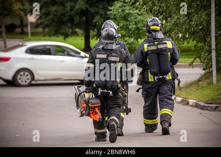 a group of three brave firefighters walking along the street in uniform and with equipment. rear view, blurred background. Stock Photo