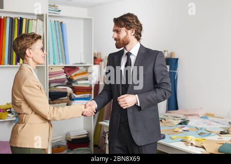 Bearded businessman in suit shaking hand with designer they greeting each other in workshop Stock Photo