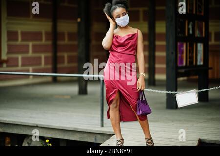Covid-19, infectious virus. African woman with curly hair, wears red silk dress and medical disposable mask, cares about her health and protects in da Stock Photo