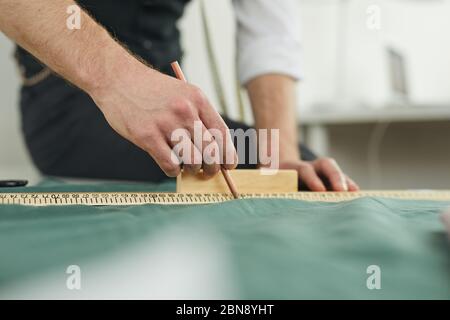 Close-up of designer using ruler and drawing on textile while sewing the clothes Stock Photo