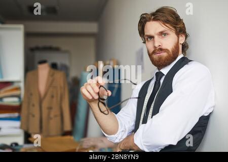 Portrait of young bearded man leaning on the wall and looking at camera in the workshop Stock Photo