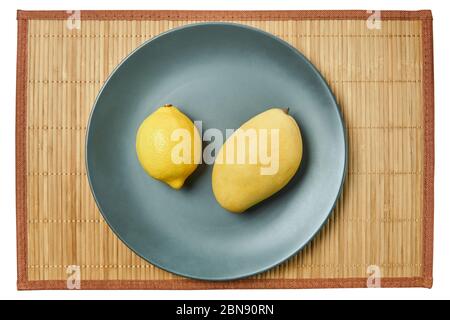 color still life - bright yellow lemon and pale yellow mango fruit on a gray plate on a cane tablecloth Stock Photo